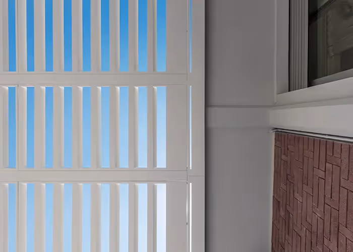 Vista dal basso delle lamelle parasole di una pergola bianca adiacente alla parete di un edificio.