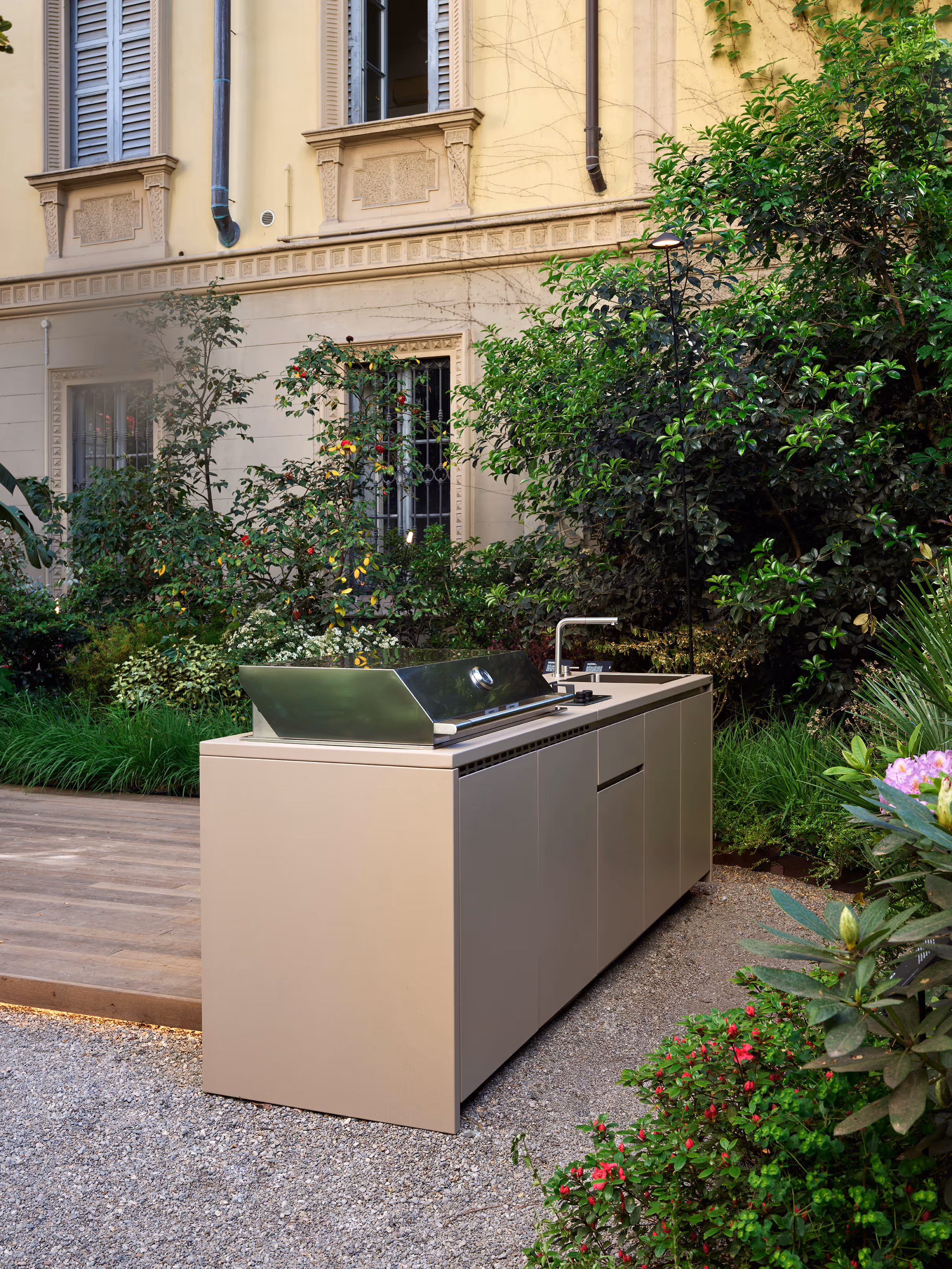 Cucina componibile da esterno color tortora con barbecue in acciaio chiuso, ambientata nel cortile di un palazzo storico.
