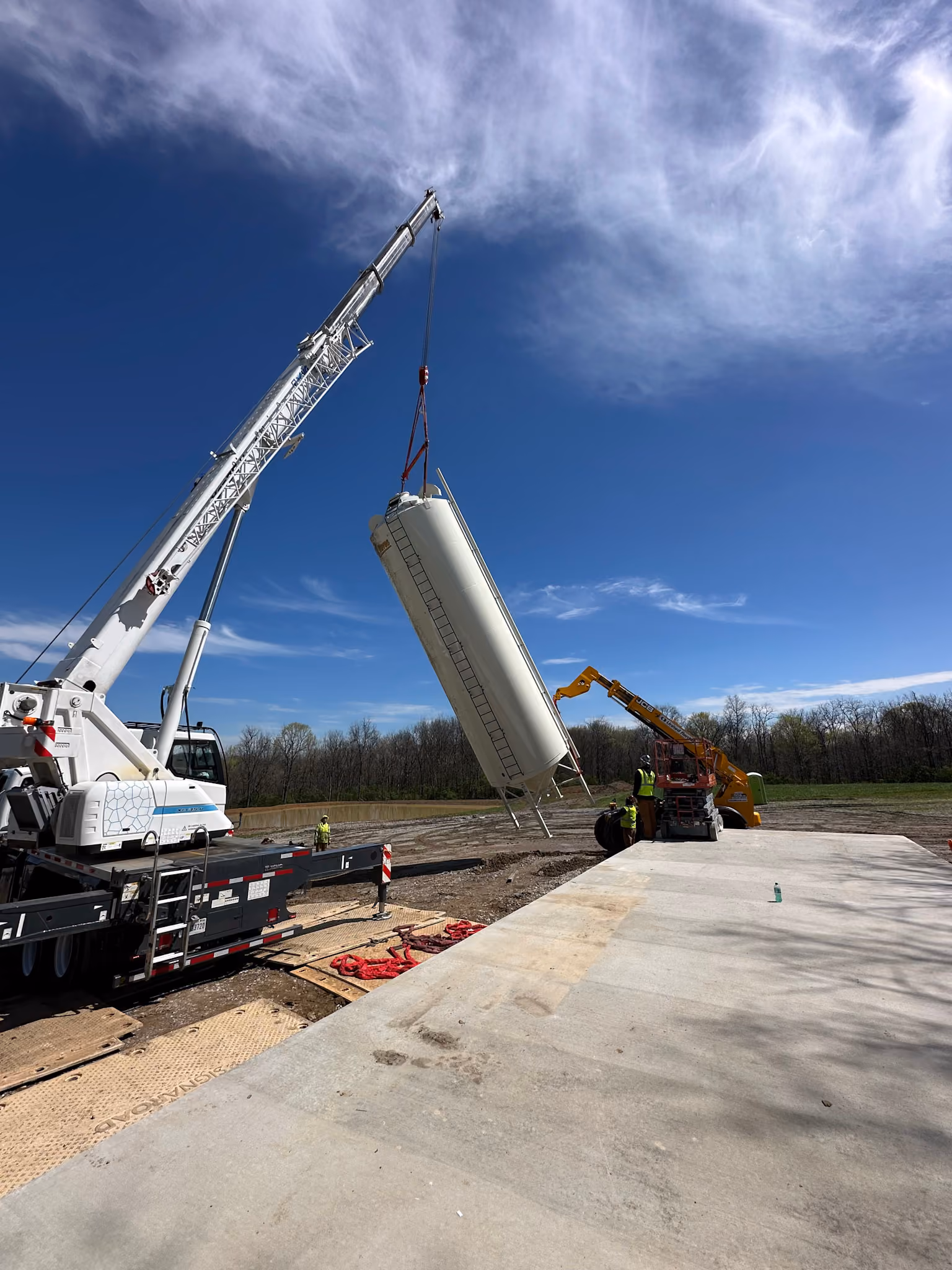 A boom truck crane lifting a silo into place at a farm