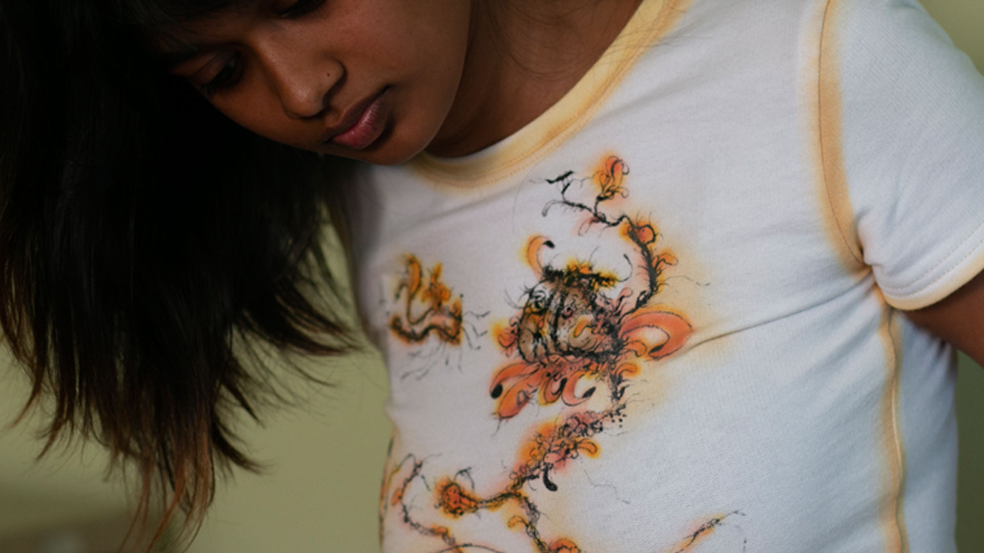 Young woman with dark hair wearing a white t-shirt with an abstract orange and black floral design.