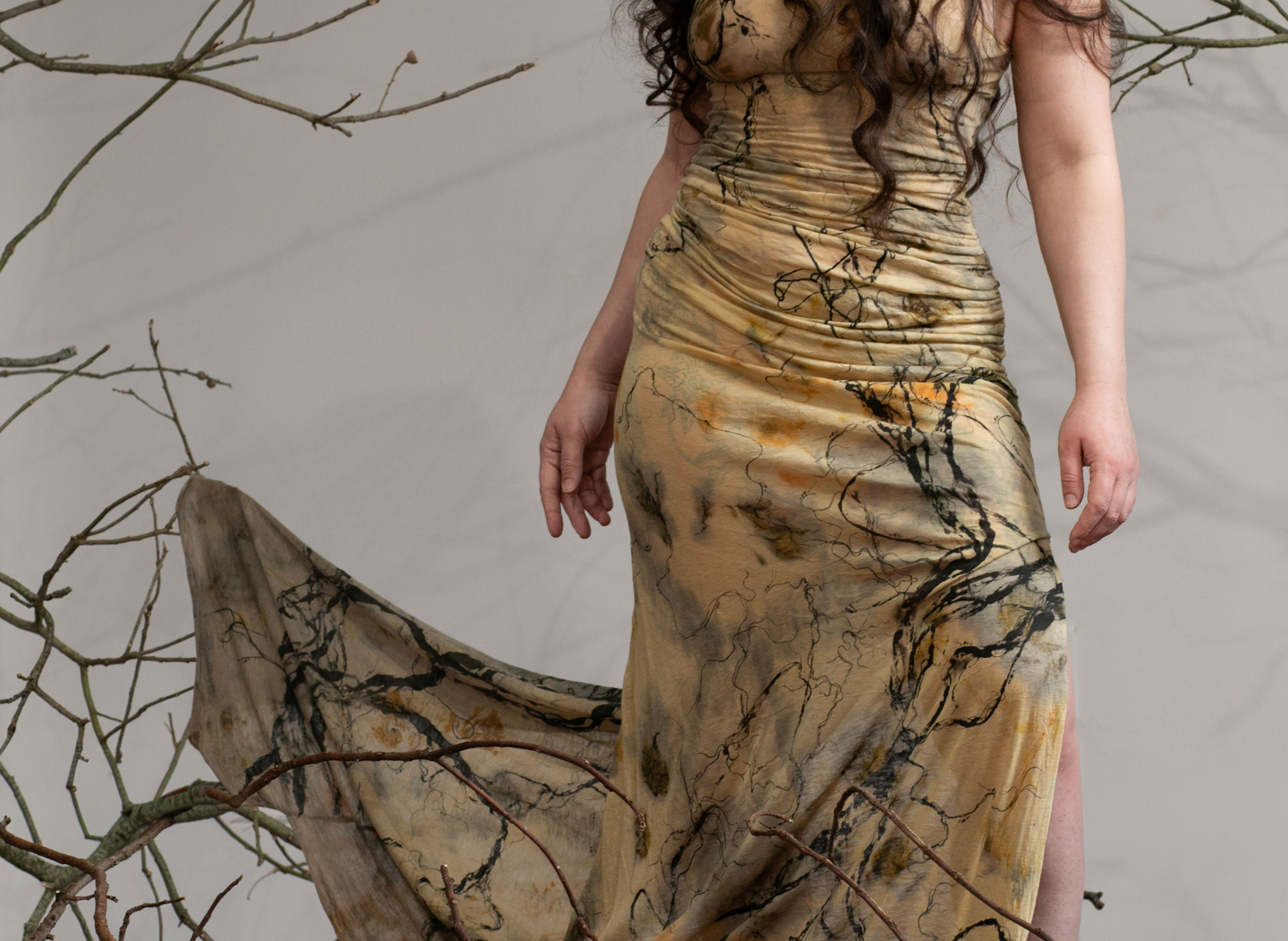 A dress caught in tree branches and a woman reaching out to untangle it 