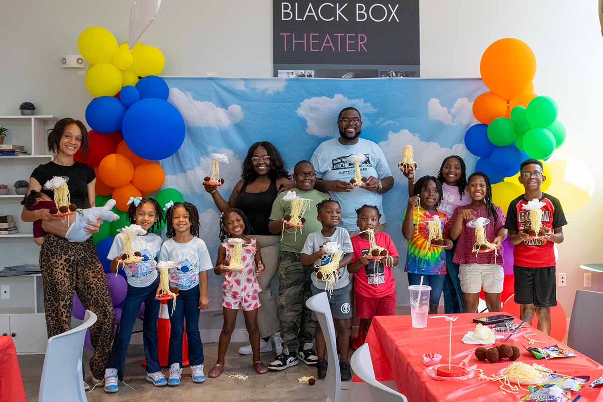 A group of 14 children, parents, and the facilitator show off their "Cloudy With a Chance of Meatballs" craft activity. 