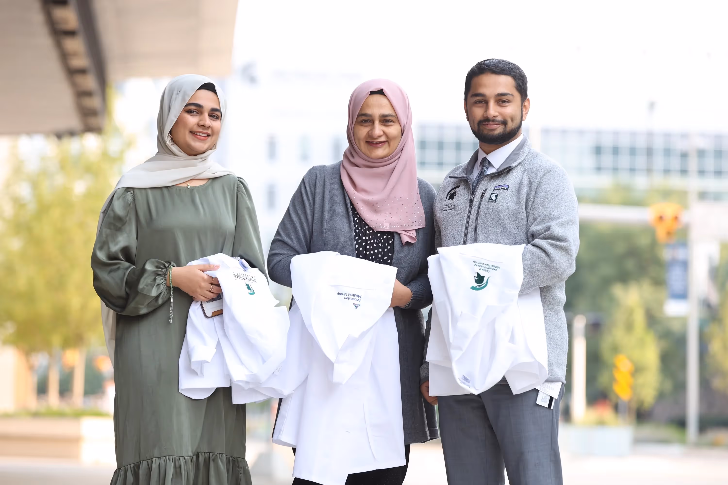 Ramsha, Humaira and Syed Rizvi pose holding their white coats after MSU medical schools ceremonies
