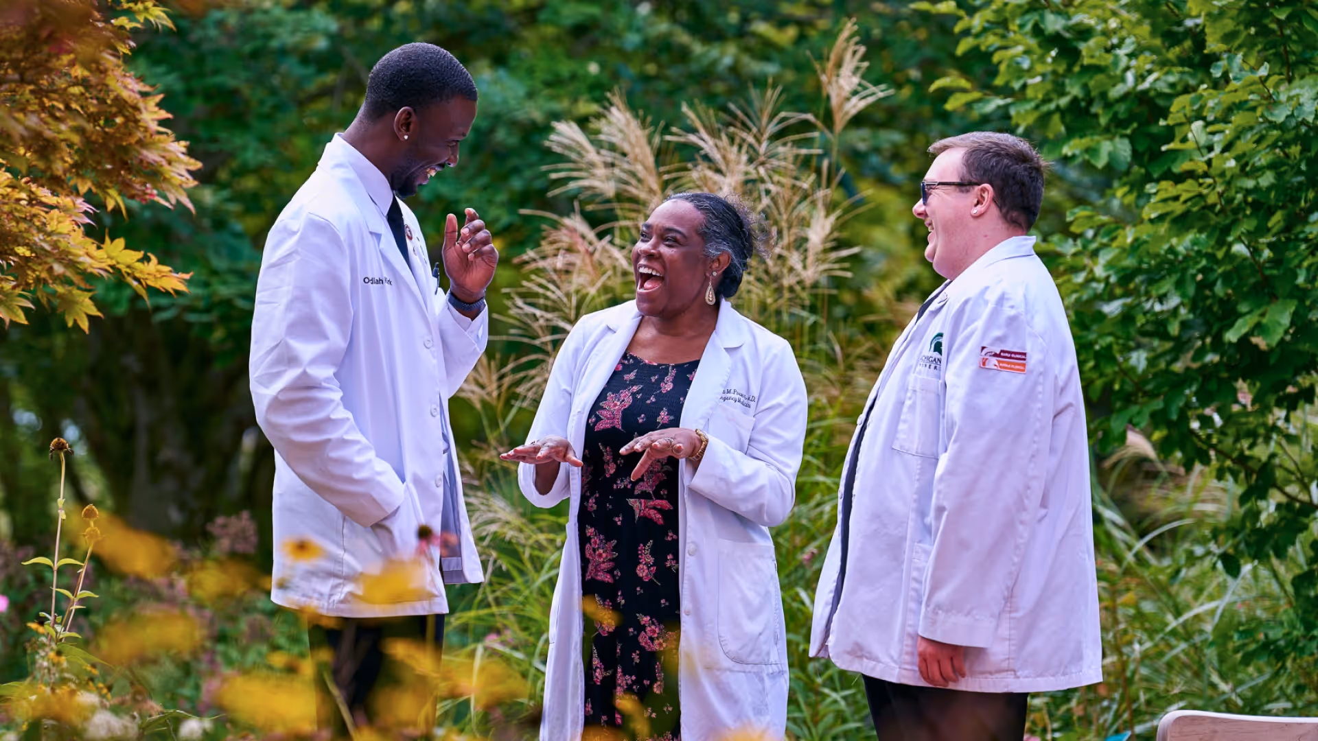 three medical professionals in white coats talking together outdoors in a garden setting