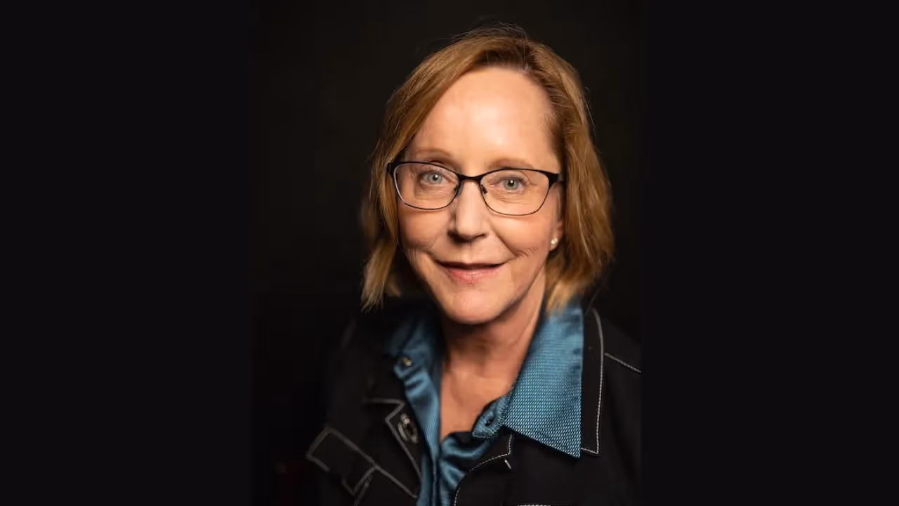 portrait photo of a person wearing a teal shirt and dark jacket against a black background