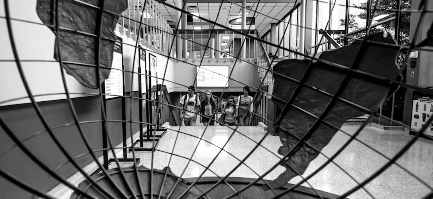 black‑and‑white image of students walking inside a school building viewed through a large globe sculpture