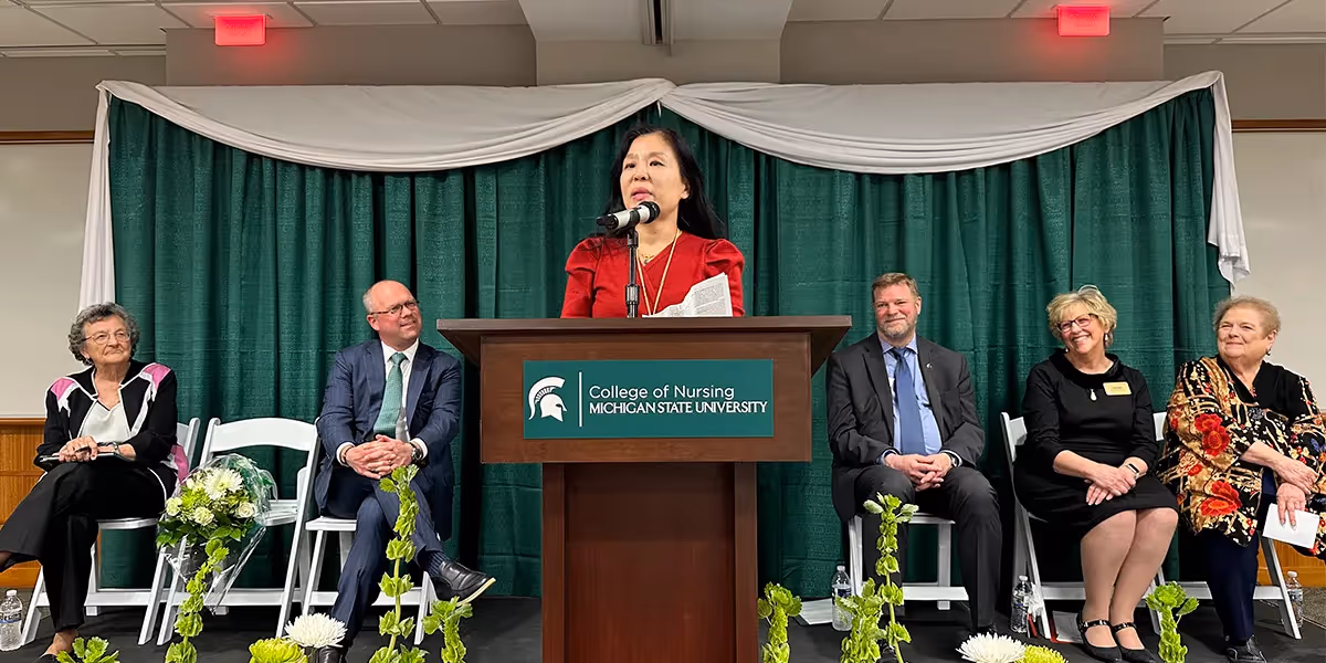 speaker addressing an audience from a podium at a College of Nursing event with panelists seated behind