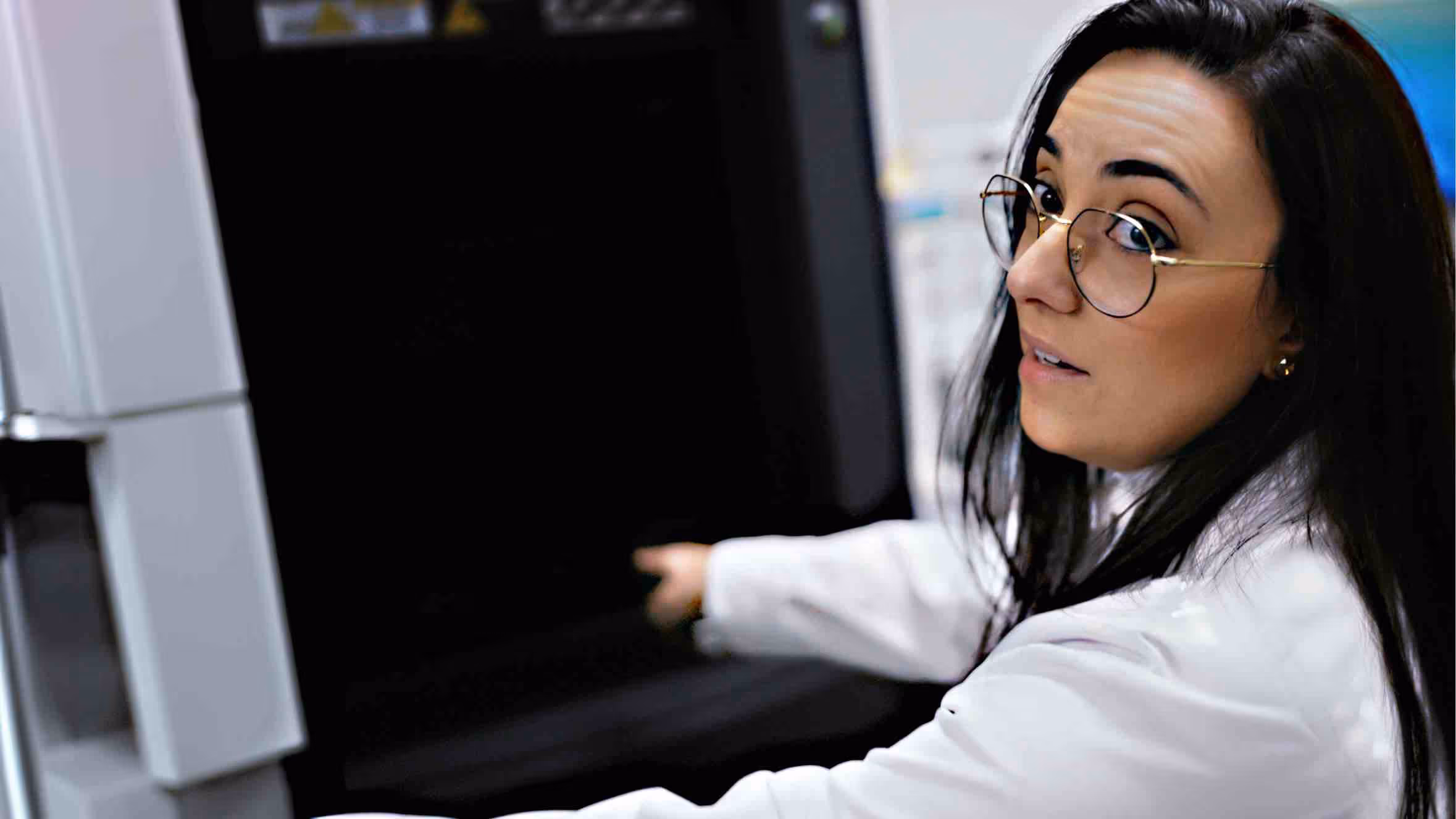 researcher in a lab coat operating large laboratory equipment inside a clinical research facility