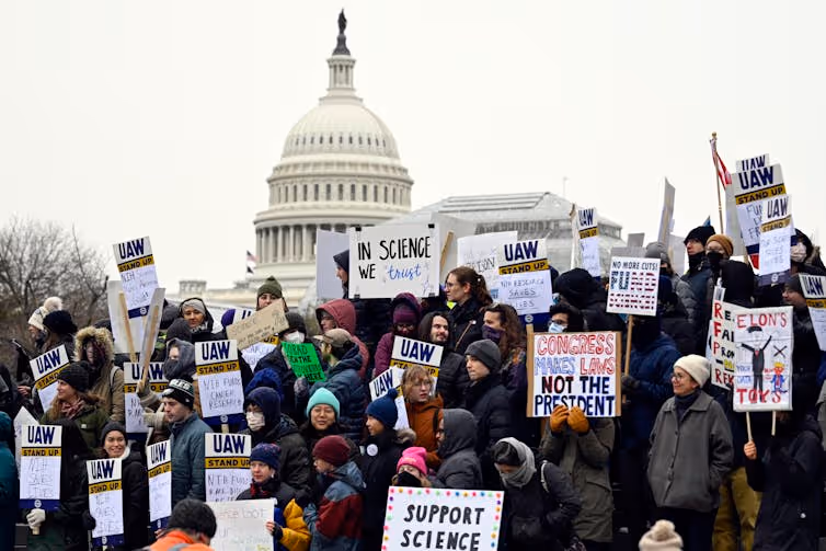 Protectors holding signs reading 'SUPPORT SCIENCE' and 'IN SCIECE WE TRUST,' among others