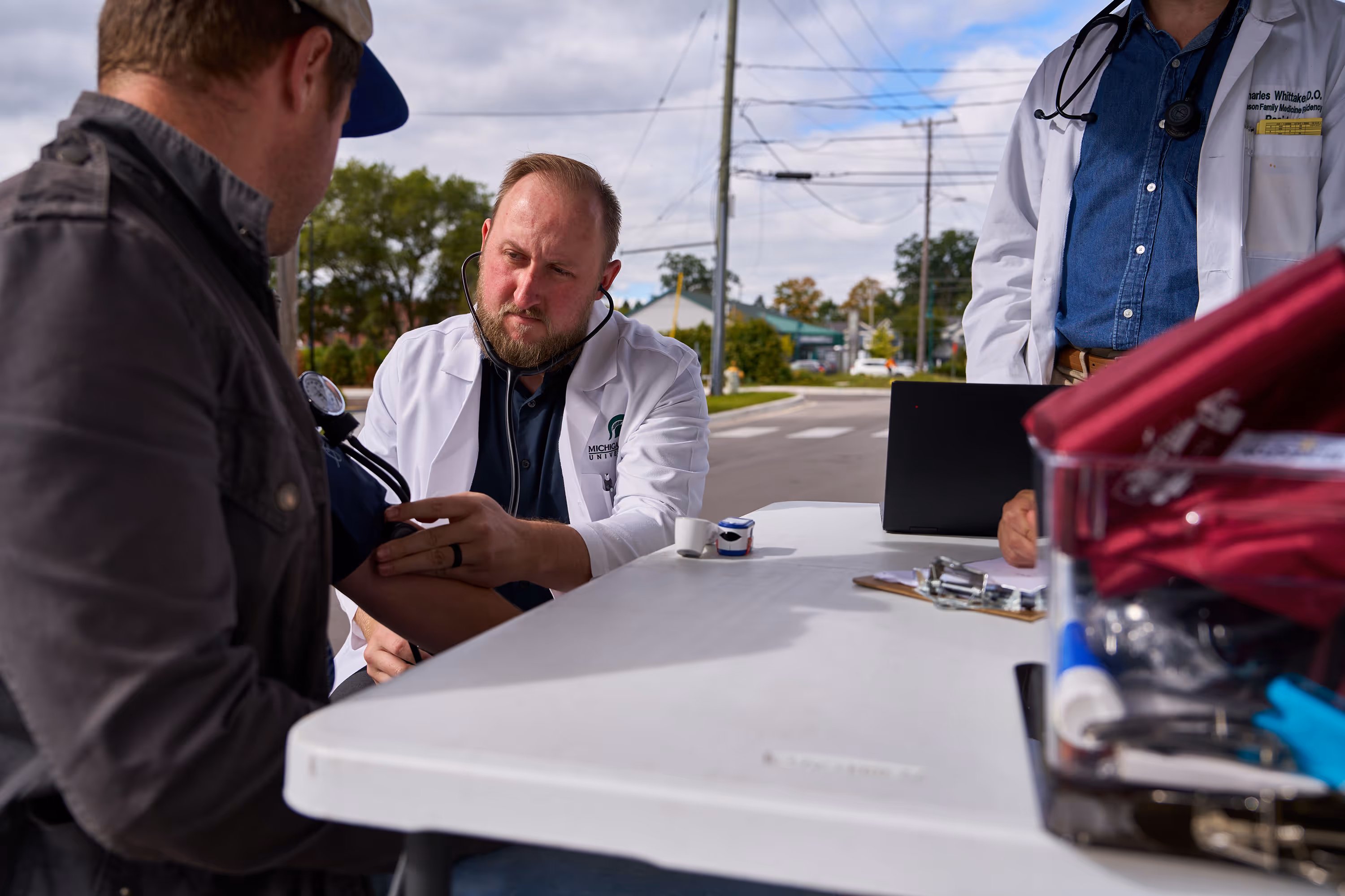 A man sitting at a table in front of the Mobile Health Clinic getting his blood pressure checked.