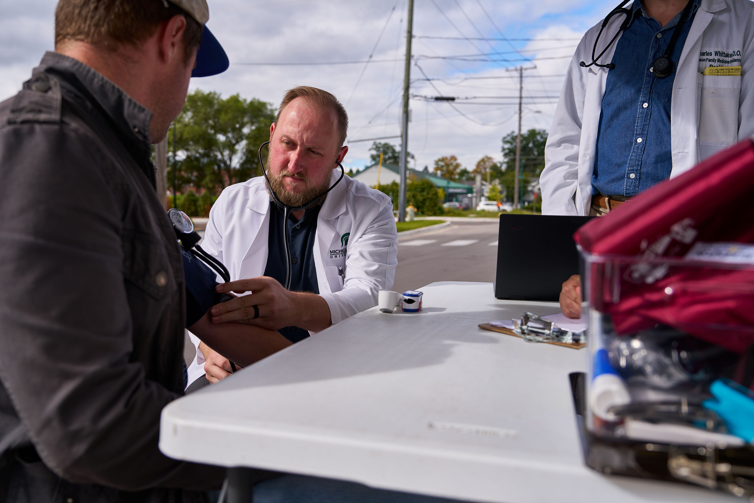 A man sitting at a table in front of the Mobile Health Clinic getting his blood pressure checked.