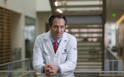 Andre Bachmann leans on a rail with hands clasped amid a blurred background.