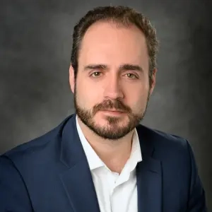 A person wearing a dark blue suit jacket and a white dress shirt against a dark gray background, suit, jacket, white dress shirt, dark gray background
