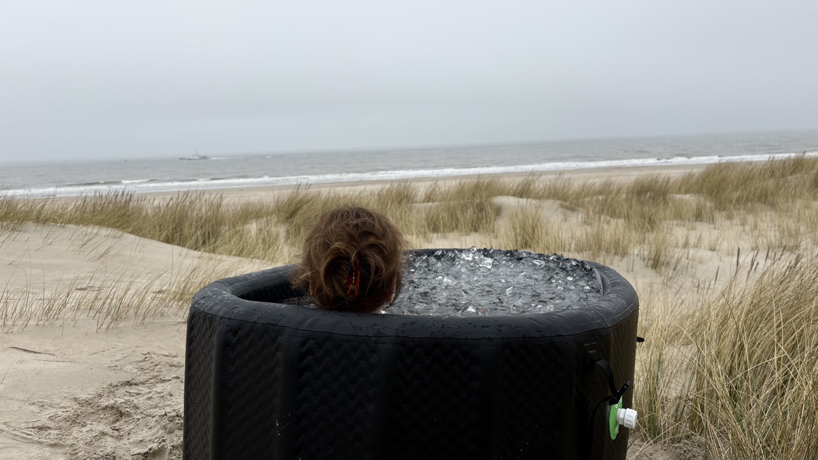 Vrouw in een ijsbad in de duinen op Vlieland, met uitzicht op het strand en de zee.