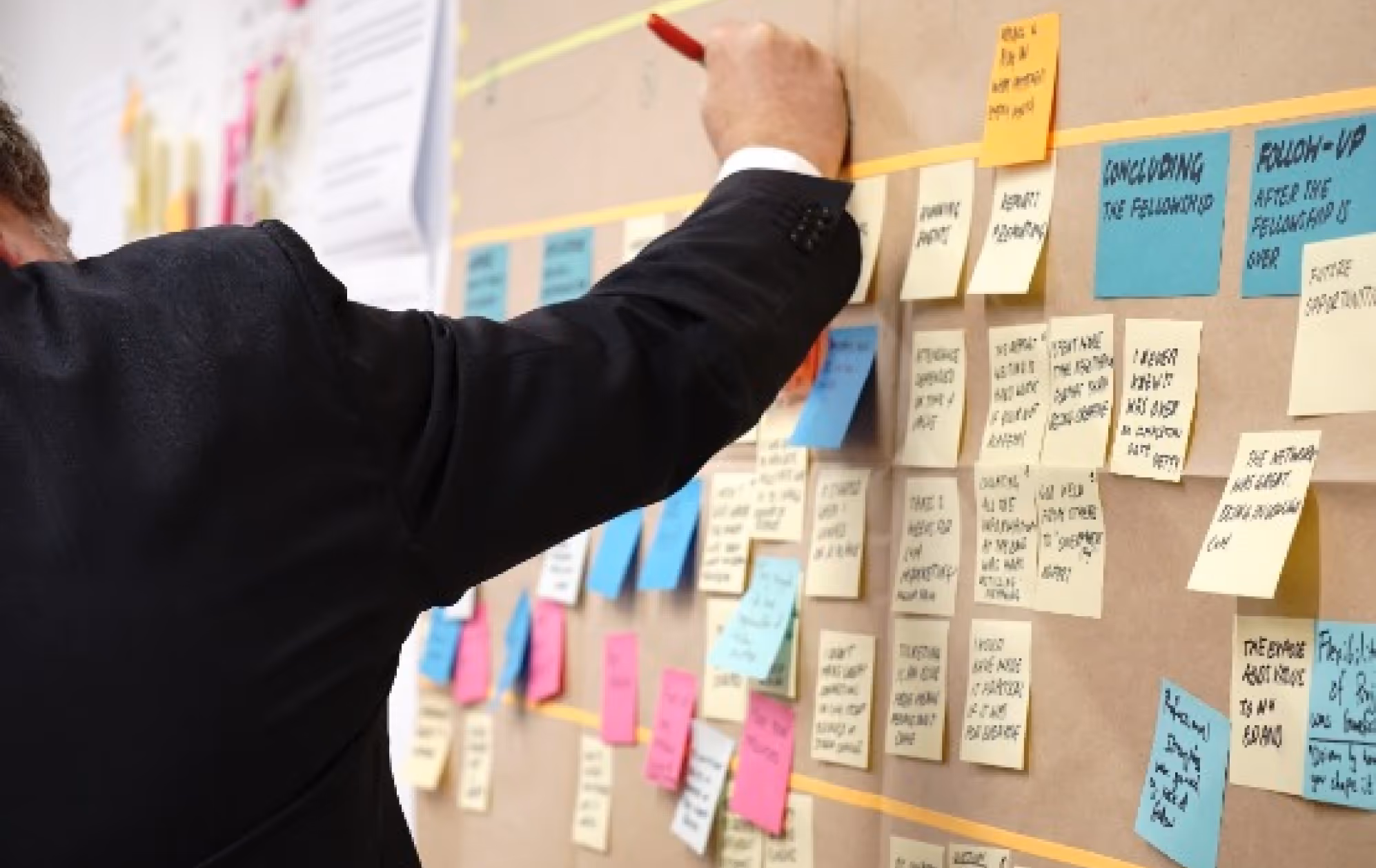 Personne qui rédige un post-it sur un mur rempli de post-it