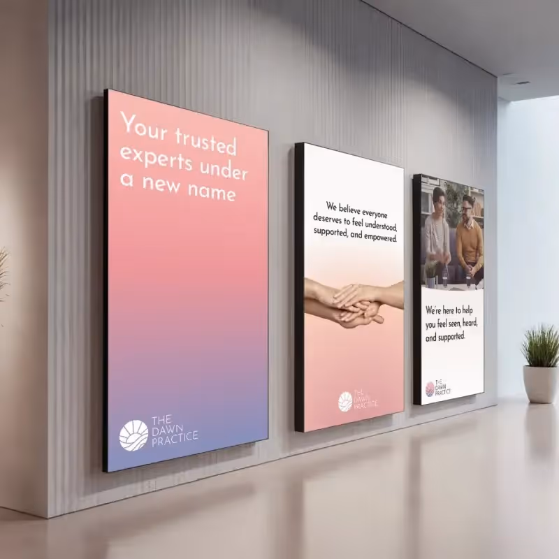 Three wall posters in a modern office: 'Your trusted experts under a new name', hands holding with text about understanding and empowerment, and two people talking with text about feeling seen and supported.