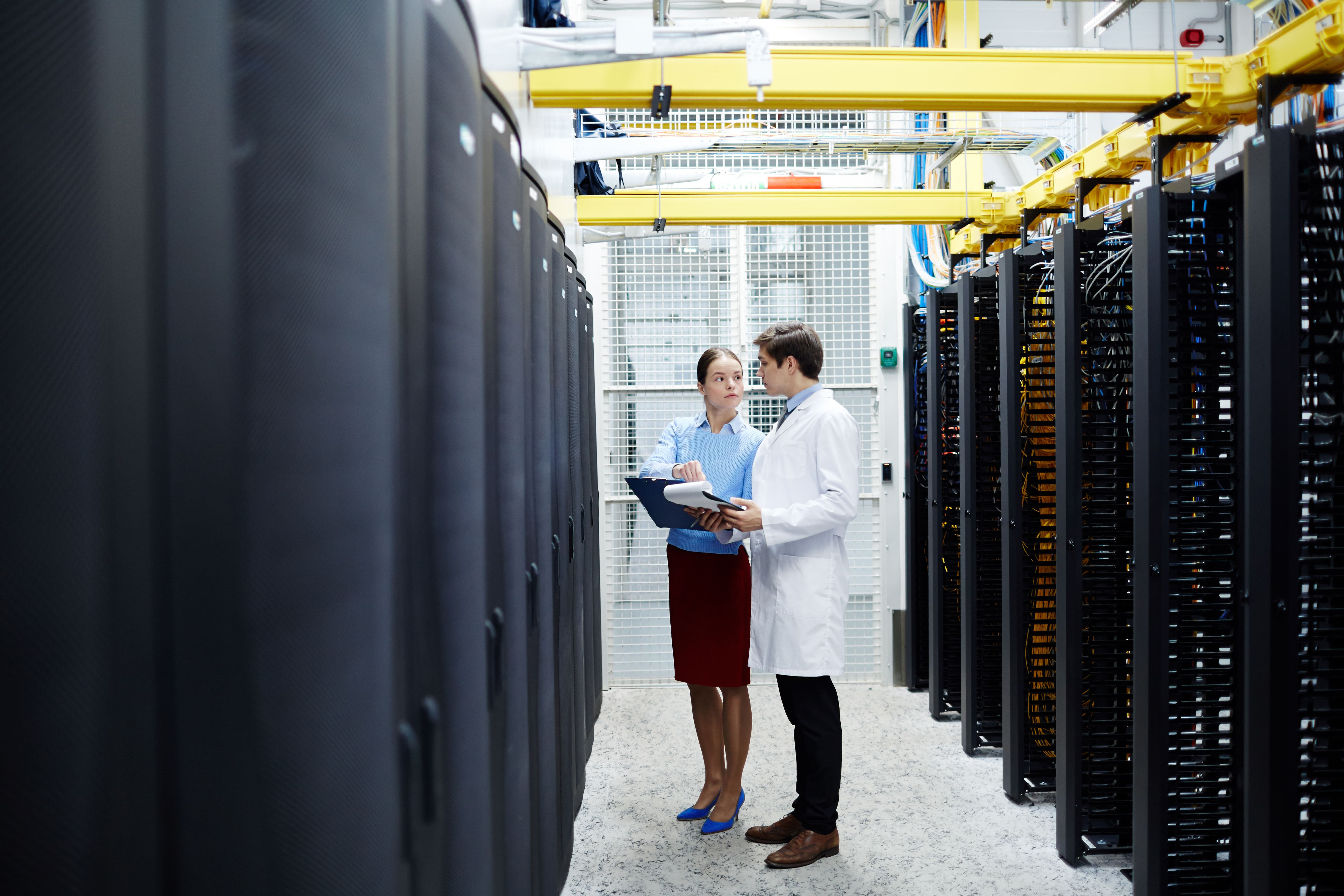 Two engineers inside a server room monitoring and inspecting the physical servers. ITAD services in Singapore take inventory before decommissioning.