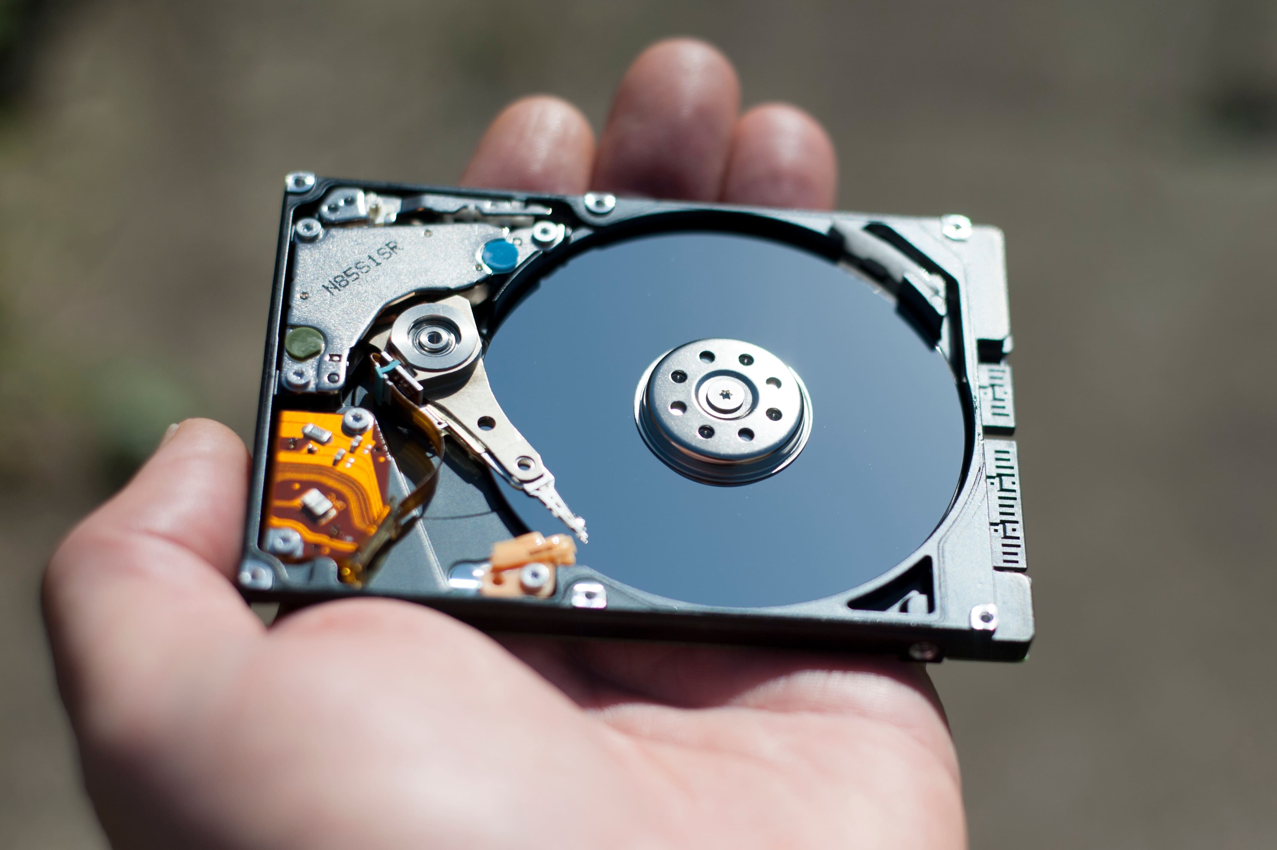 Hand holding an open hard drive outdoors, showing the disk platter and actuator arm