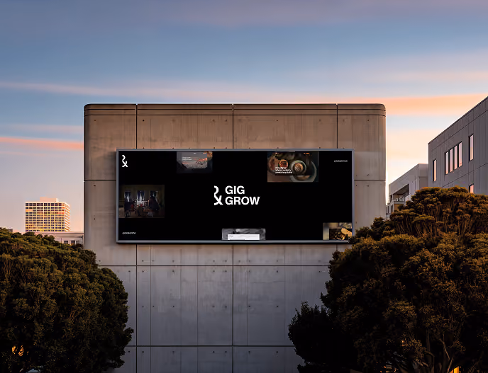 Outdoor digital billboard on concrete building at sunset displaying 'GIG GROW' with small images.