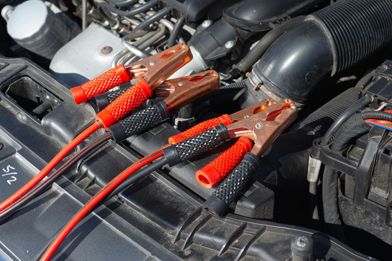 Close-up of copper jumper cable clamps connected to car battery terminals inside engine bay during vehicle jump starting procedure outdoors.
