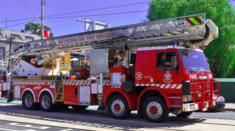 Red Metropolitan Fire Brigade ladder truck parked roadside, featuring extended aerial ladder, emergency rescue equipment, and multiple heavy-duty axles.