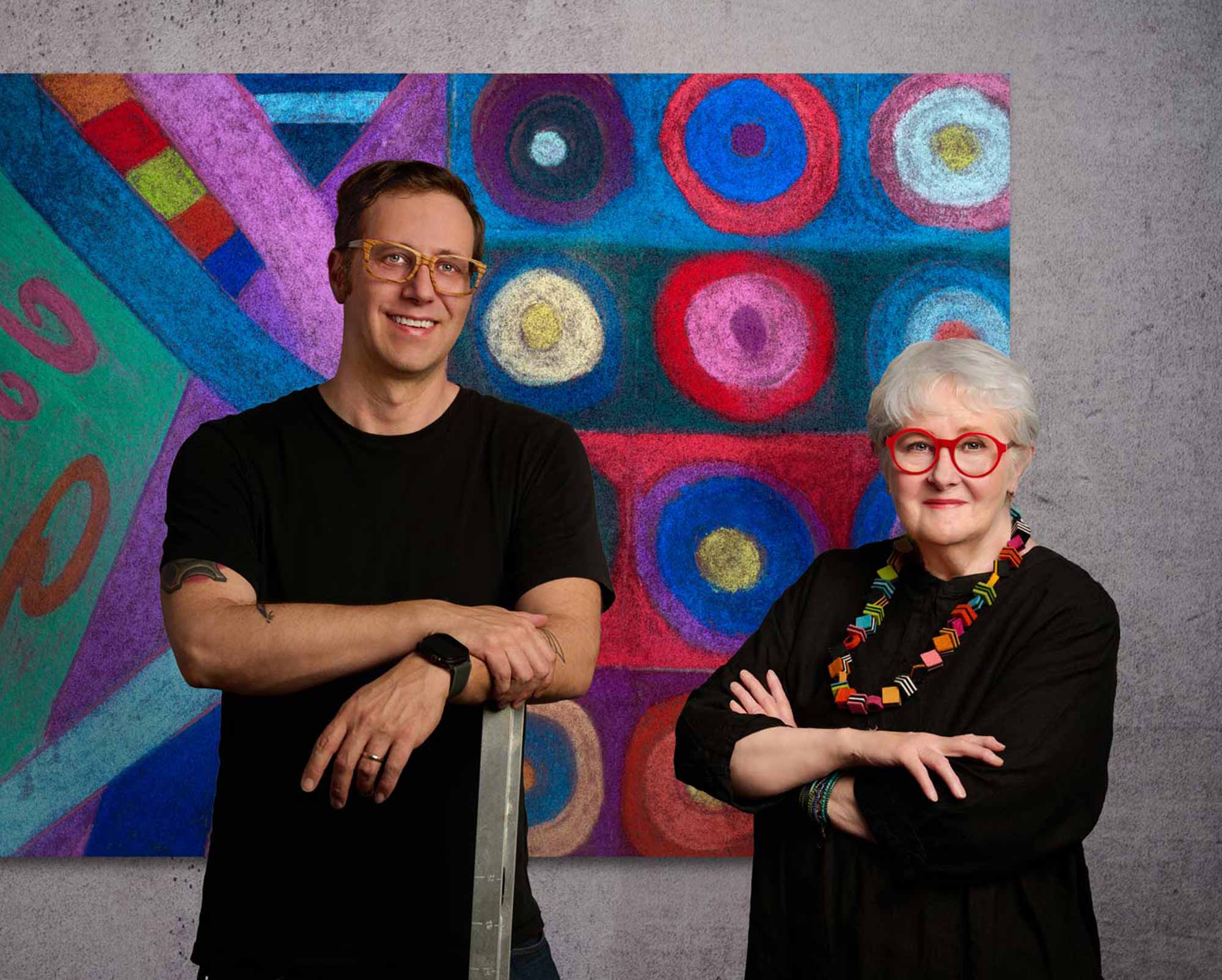 A Photo of a Man and a Woman standing in front of a vibrant piece of children's artwork printed large and installed on the wall in an office.