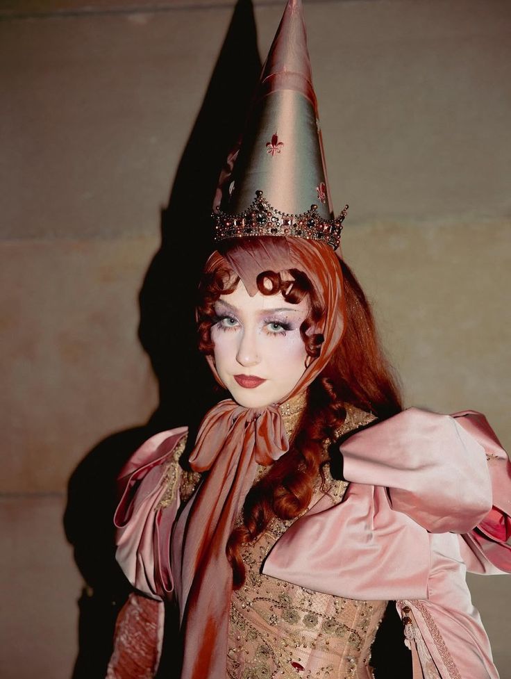 This may contain: a woman with red hair wearing a pink dress and a silver hat