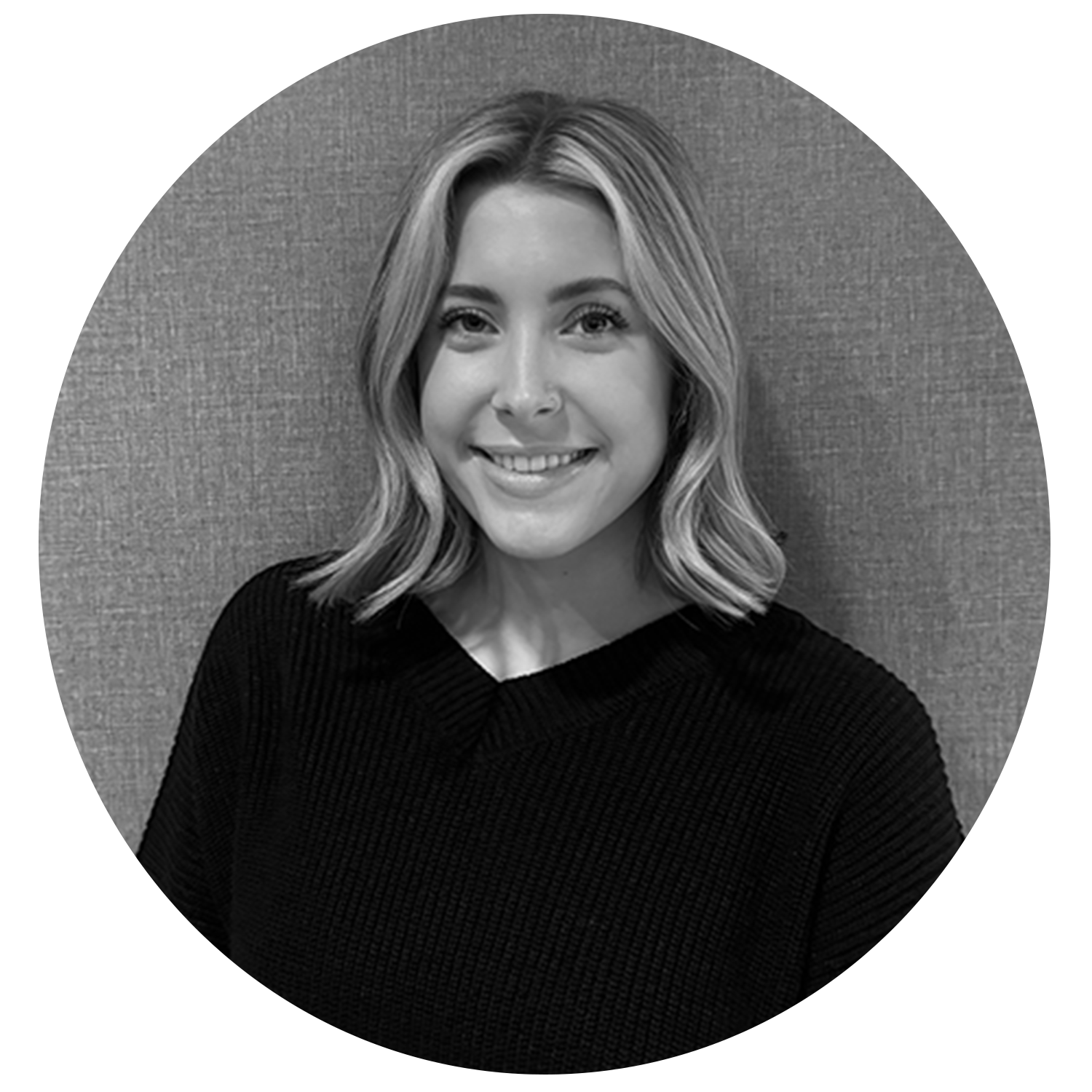 Smiling woman with shoulder-length wavy hair wearing a black sweater against a textured background.