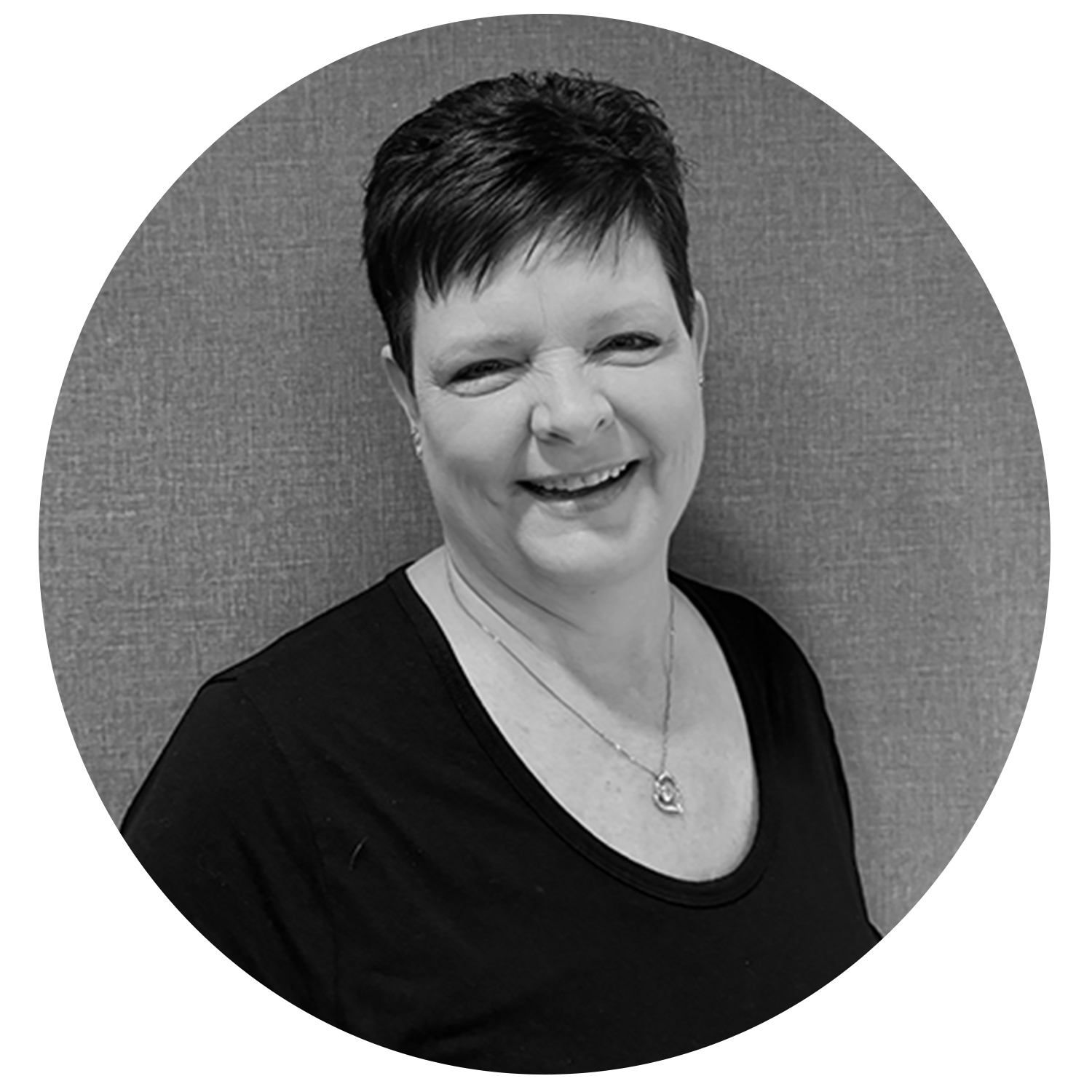 Smiling woman with short dark hair wearing a black top and necklace, posing against a textured background.