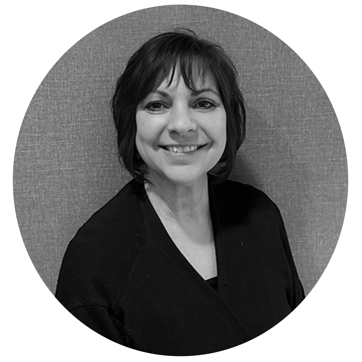 Smiling woman with short dark hair wearing a dark top, standing against a textured wall.