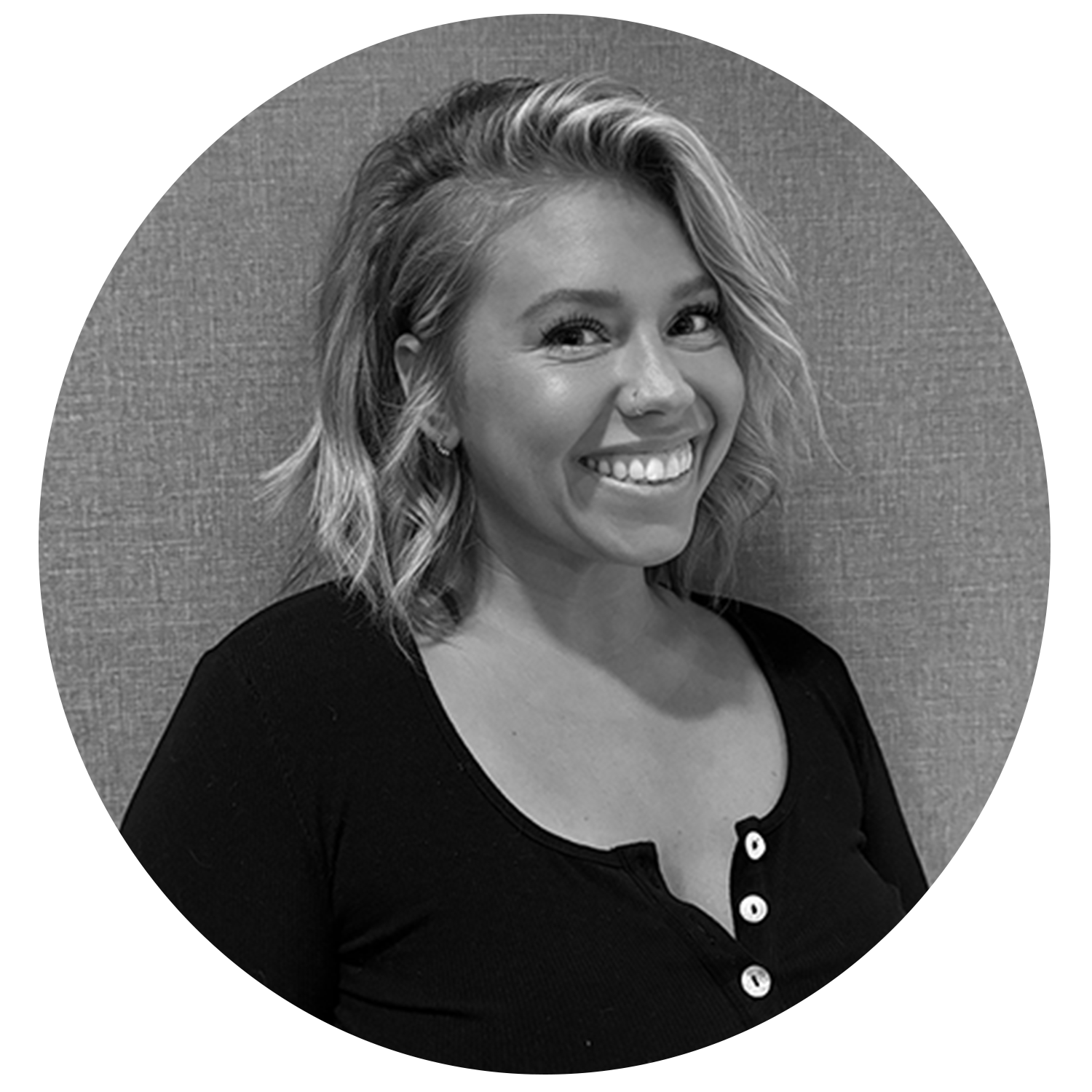 Smiling woman with shoulder-length wavy hair wearing a black buttoned top against a textured background.