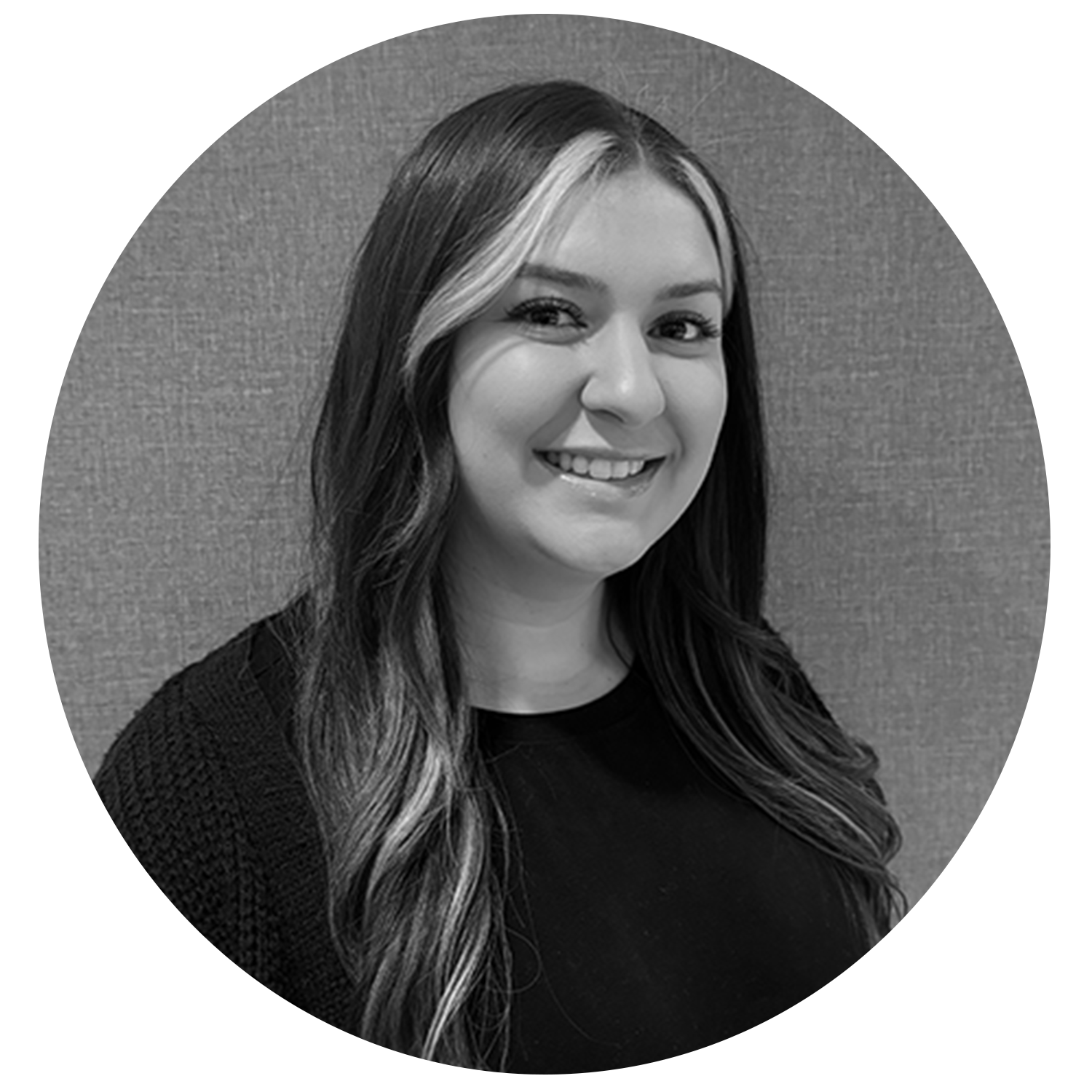 Smiling woman with long wavy hair and light highlights posing against a textured wall.