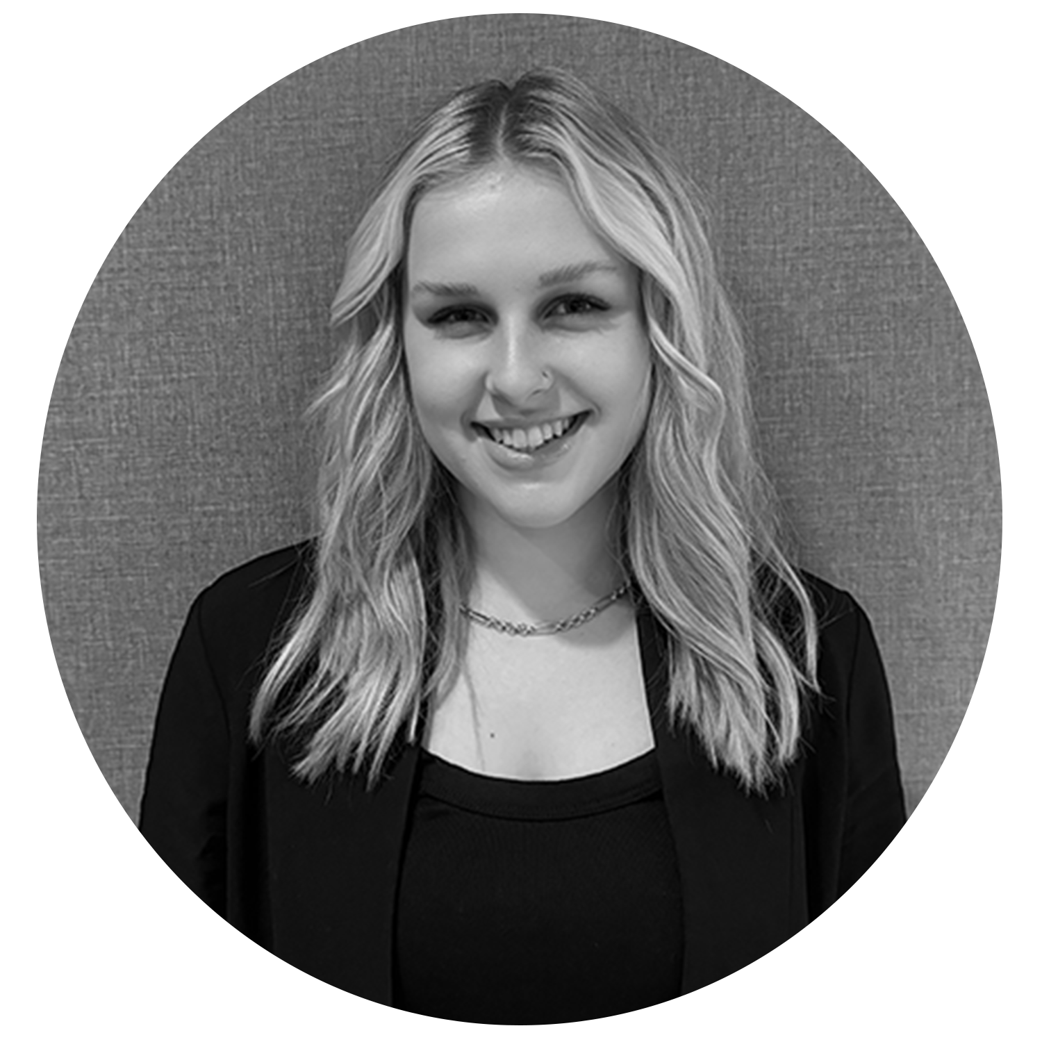 Smiling woman with wavy blonde hair wearing a black top and blazer, standing against a textured background.