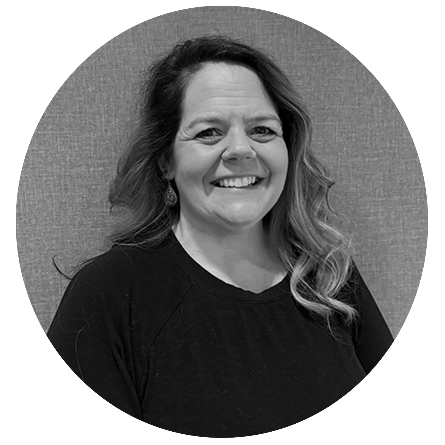 Smiling woman with wavy hair wearing a black top and teardrop earrings against a textured background.