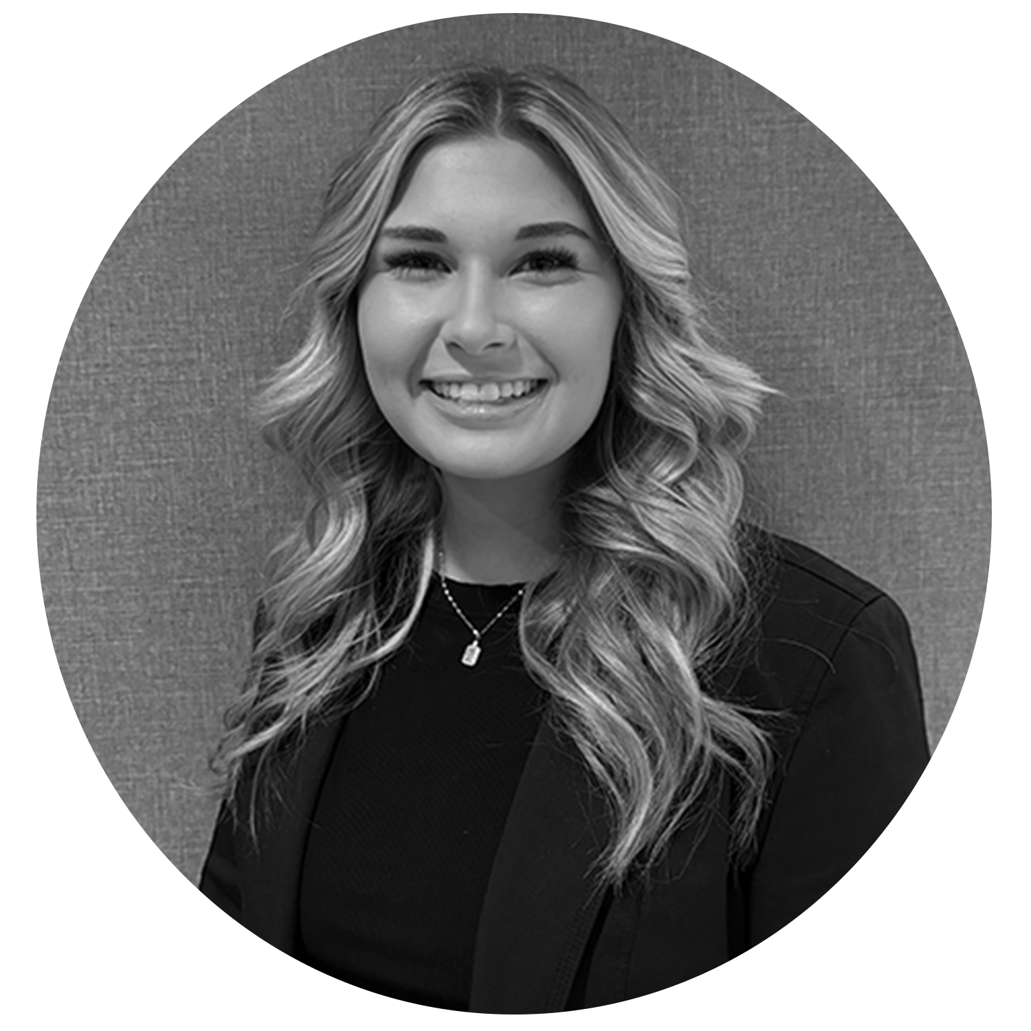 Smiling young woman with long wavy hair wearing a black top and blazer against a textured background.