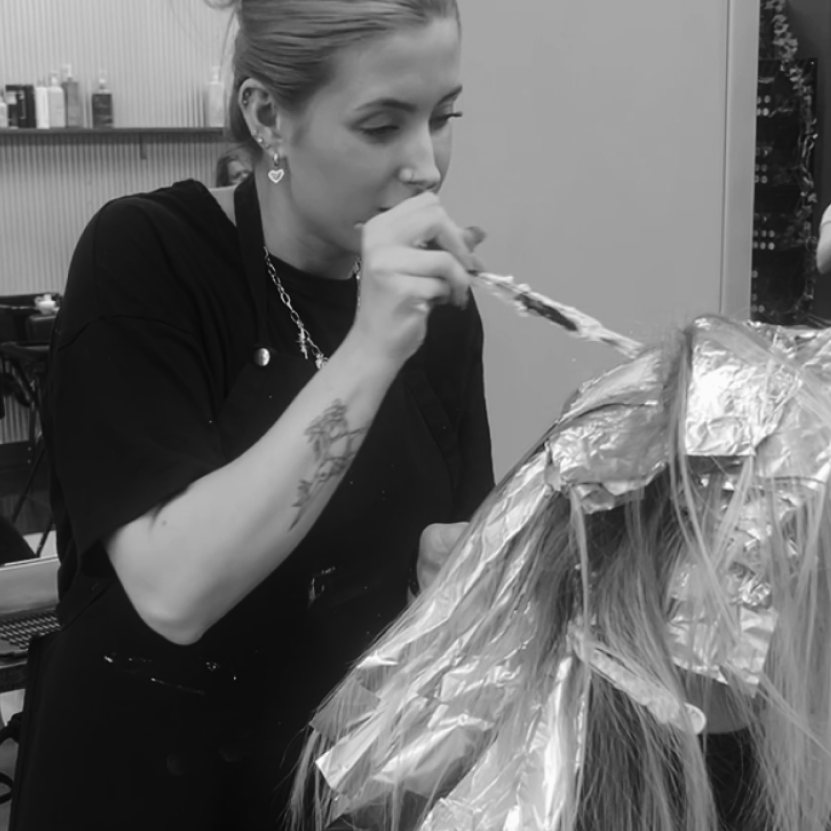 Hairstylist applying hair color with brush to a client's hair wrapped in foil sheets.