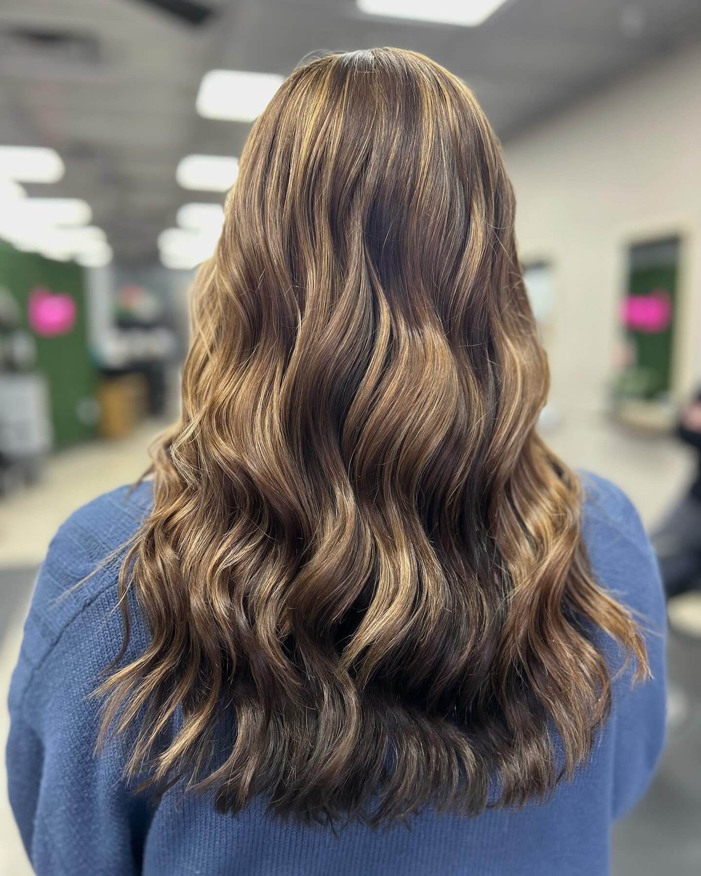 Back view of shoulder-length wavy hair with blonde highlights worn by a person in a blue sweater.