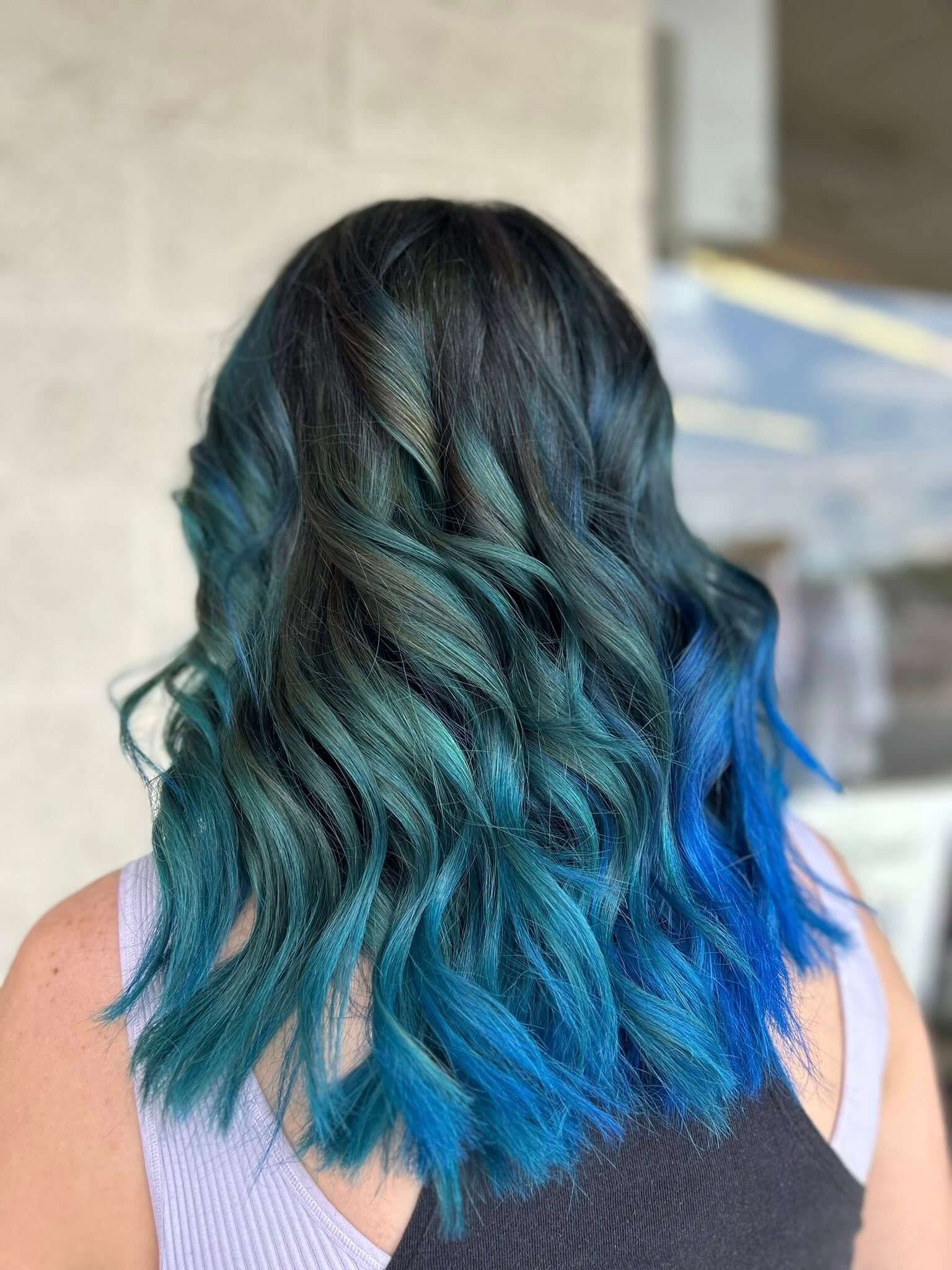 Back view of shoulder-length wavy hair dyed in gradient shades of dark green transitioning to bright blue.