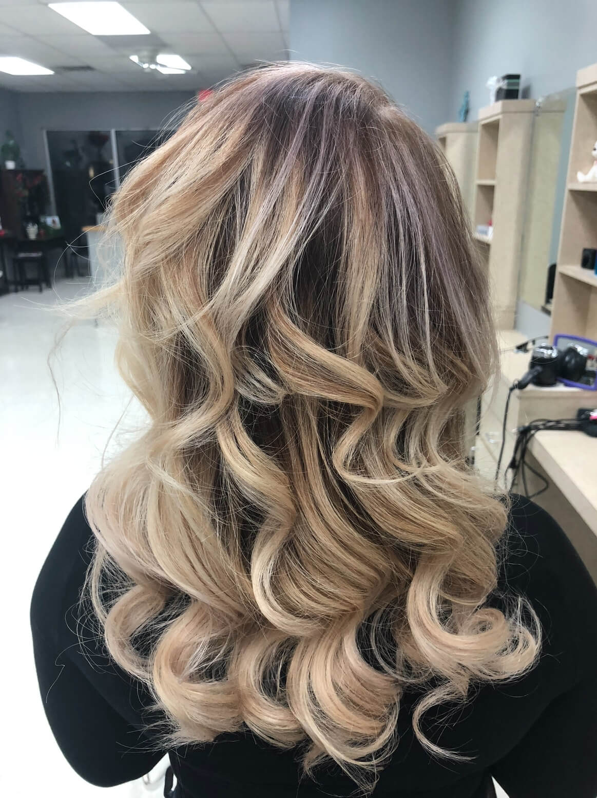 Back view of styled medium-length wavy hair with blonde highlights in a salon setting.