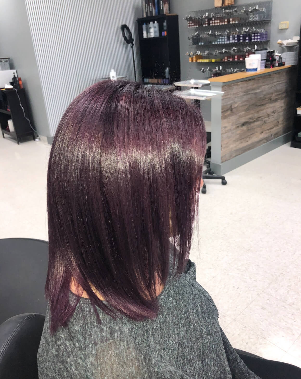 Woman with sleek, straight, shoulder-length dark purple hair sitting in a salon chair.