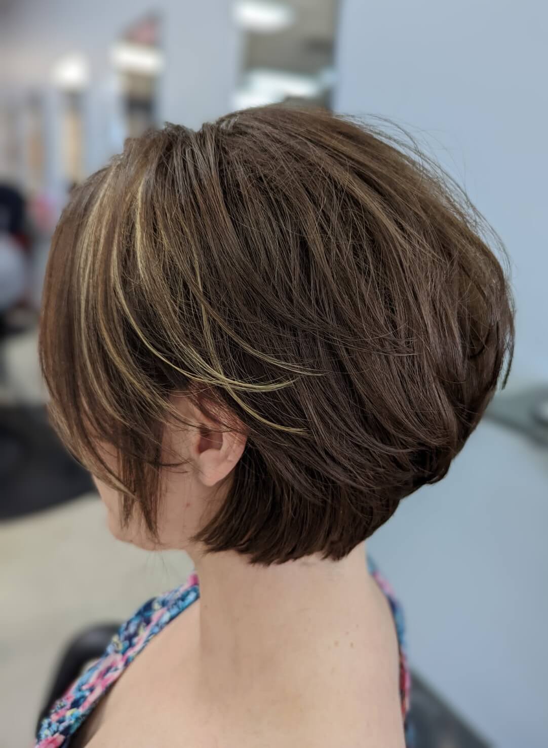 Side view of a person with short layered brown hair featuring subtle blonde highlights in a salon setting.
