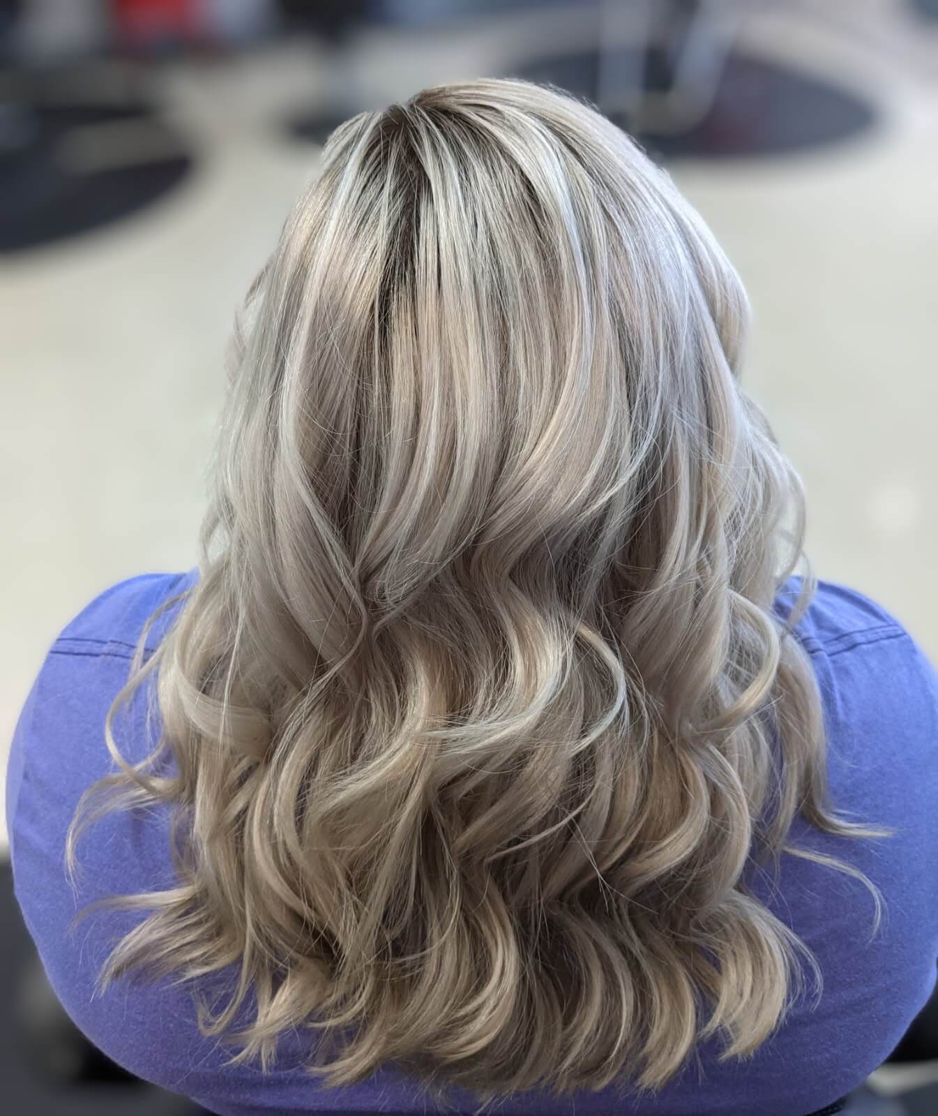 Back view of a person with shoulder-length wavy blonde hair with darker roots wearing a purple top.