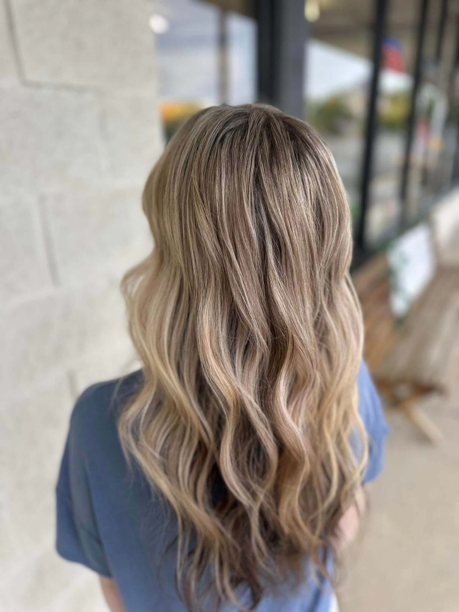 Woman with long, wavy blonde hair viewed from the back wearing a blue shirt.