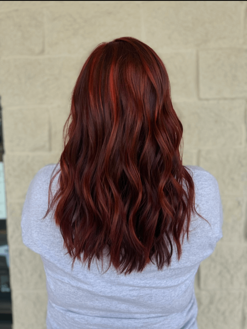 Back view of a person with medium-length wavy dark red hair wearing a light gray shirt.
