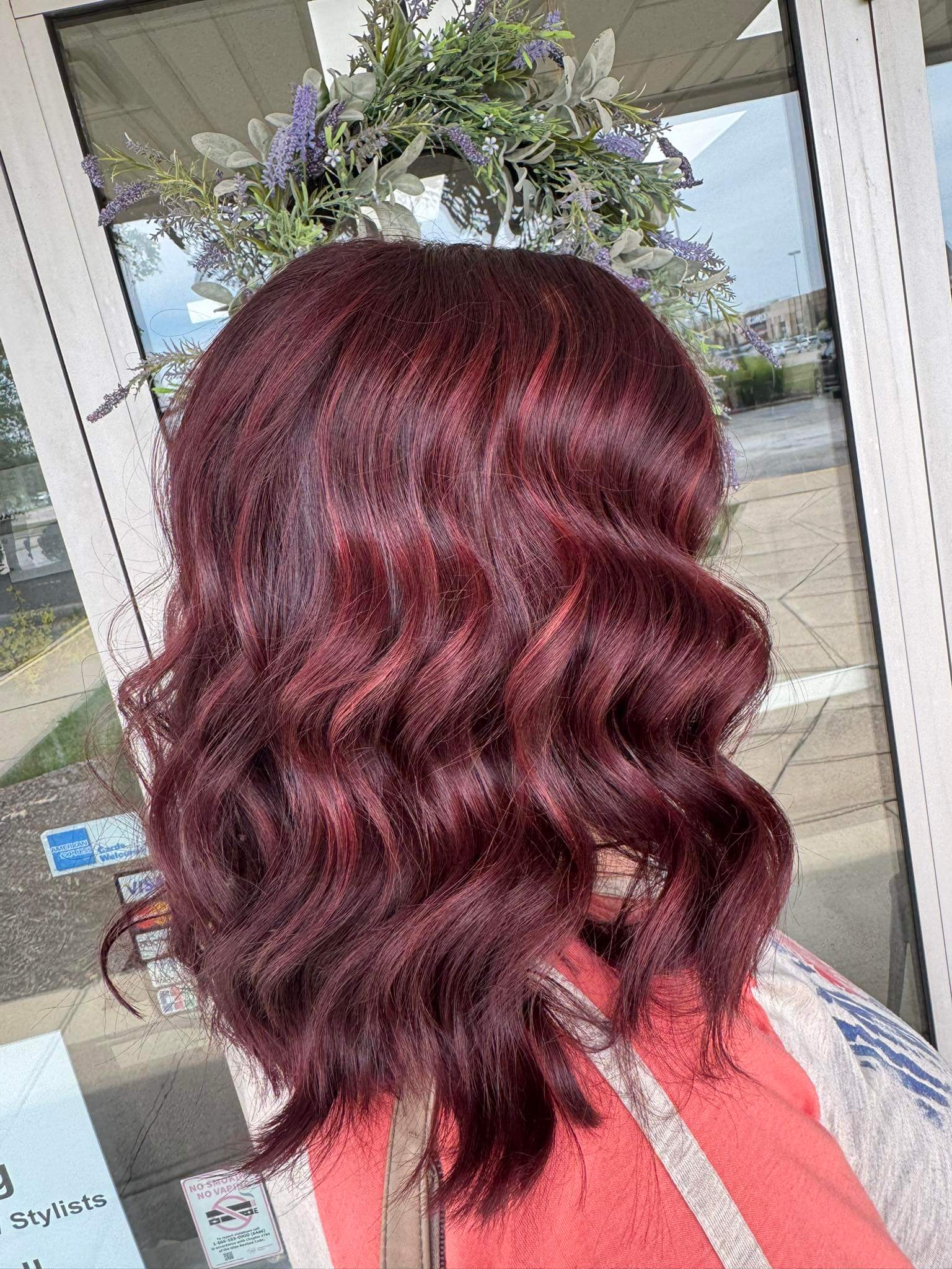 Person with long, wavy magenta hair seen from the back in a salon setting.