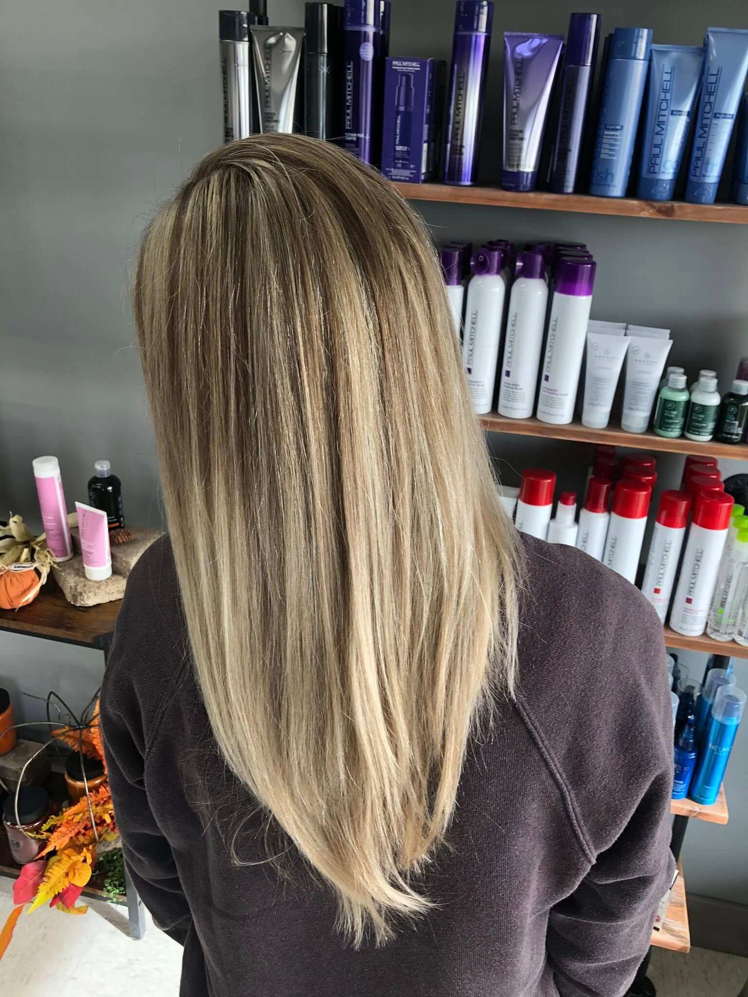 Back view of a person with long, straight, blonde hair standing in front of shelves filled with hair care products.
