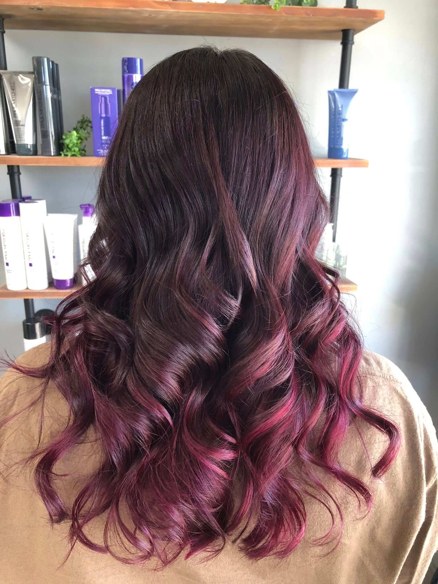 Back view of long wavy hair with dark roots fading into vibrant pink highlights.
