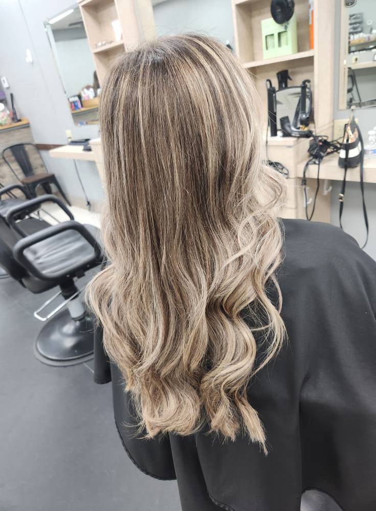 Back view of a person with long, wavy, blonde and brown highlighted hair sitting in a salon chair.