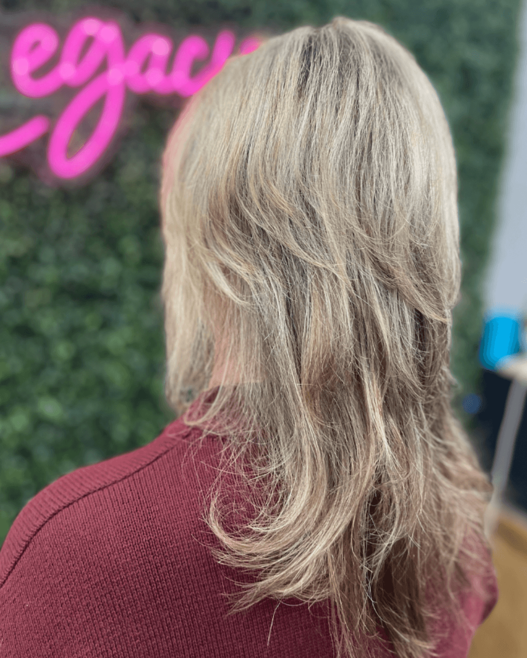 Back view of a person with layered, shoulder-length blonde hair wearing a maroon sweater.