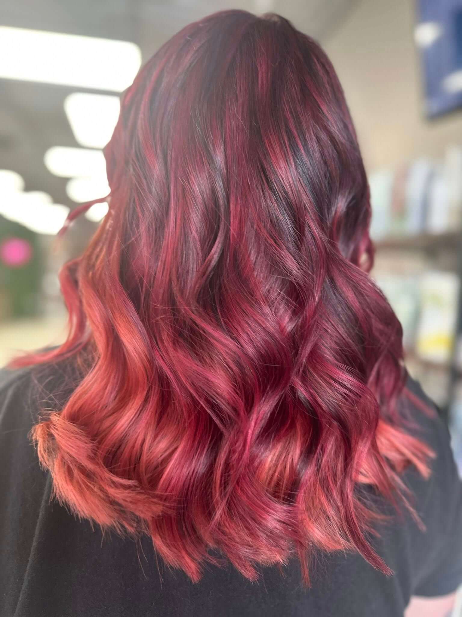 Back view of shoulder-length wavy hair dyed in shades of deep red and pink.
